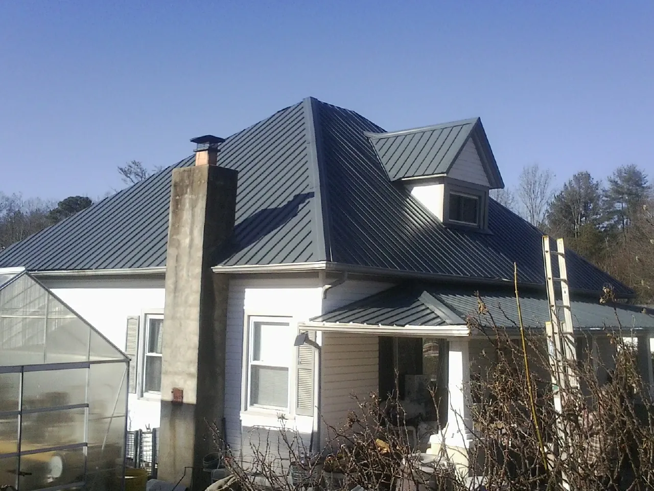 Dark blue standing seam metal roof on a white farmhouse with dormer — Slate & Tile Roof Repair by Roofing Brothers in Creswell