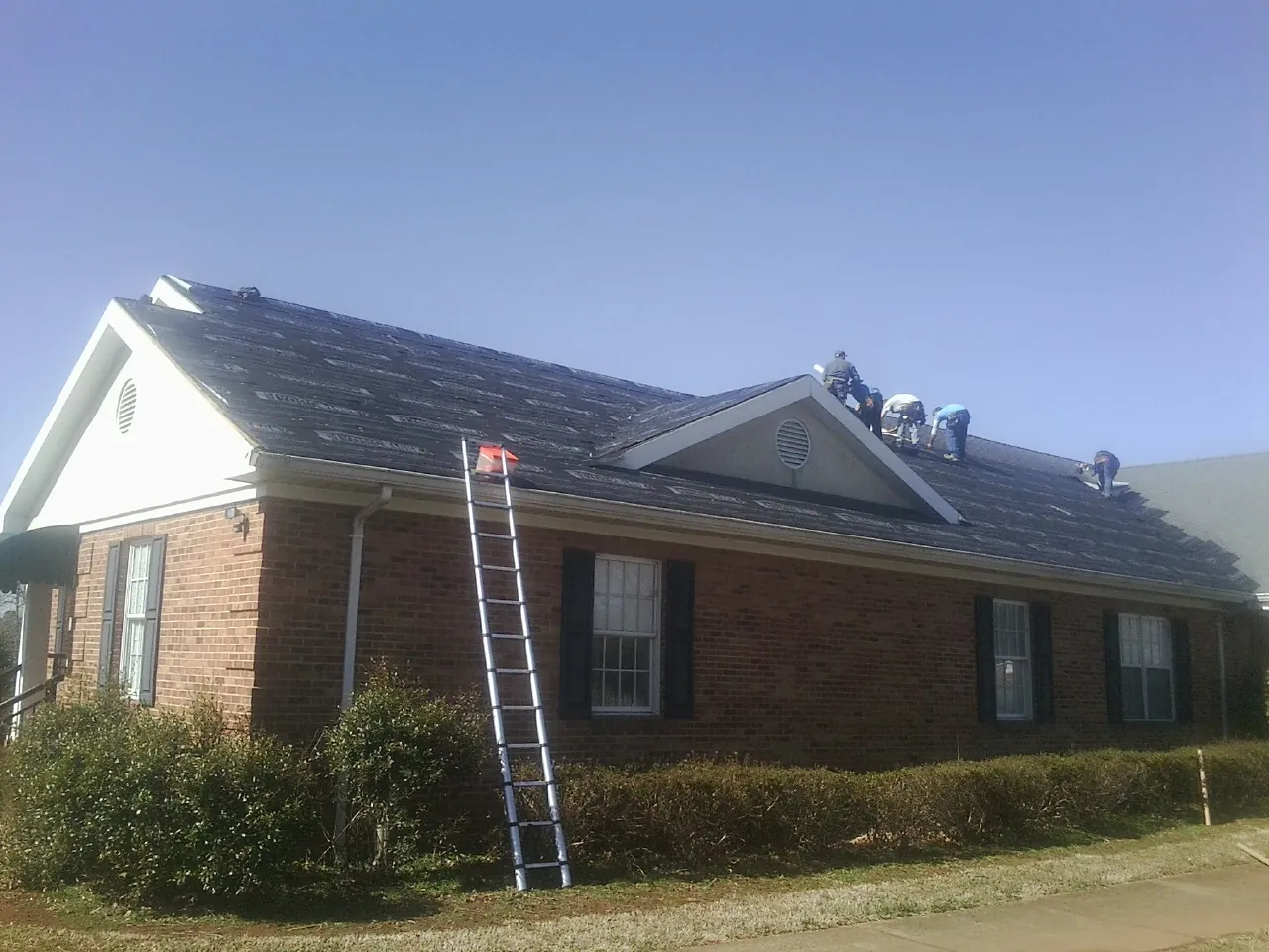 Crew tearing shingles off a brick ranch roof with a ladder set — Metal Roof Repair work by our crew in Creswell