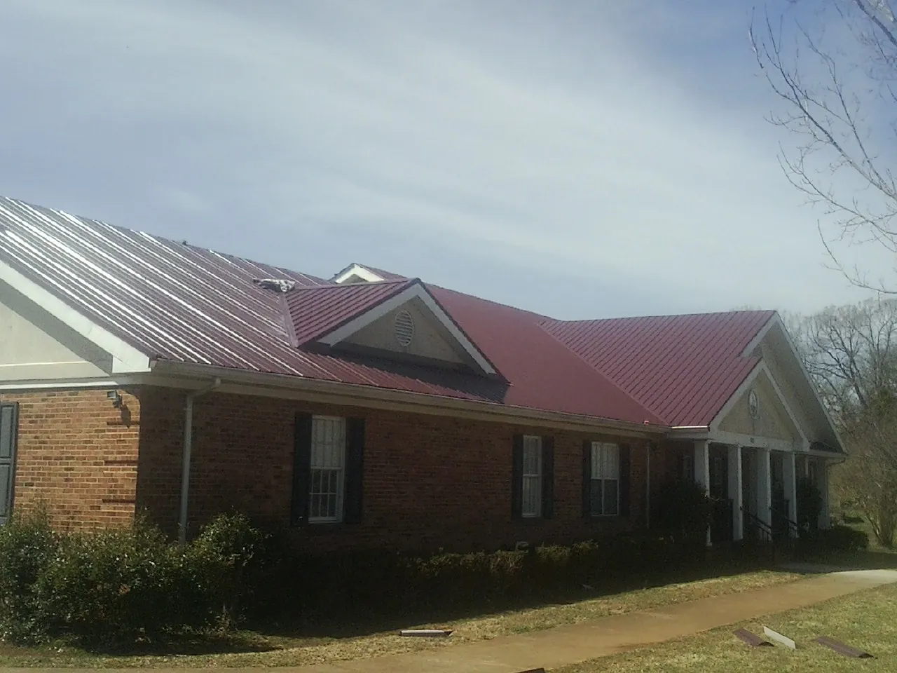 Red metal roof with gabled entries on a long brick building, from a Hail Damage Roof Repair job in Creswell