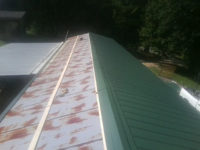 Old rusted panels beside newly installed green metal roofing — Wind Damage Roof Repair by Roofing Brothers in Creswell