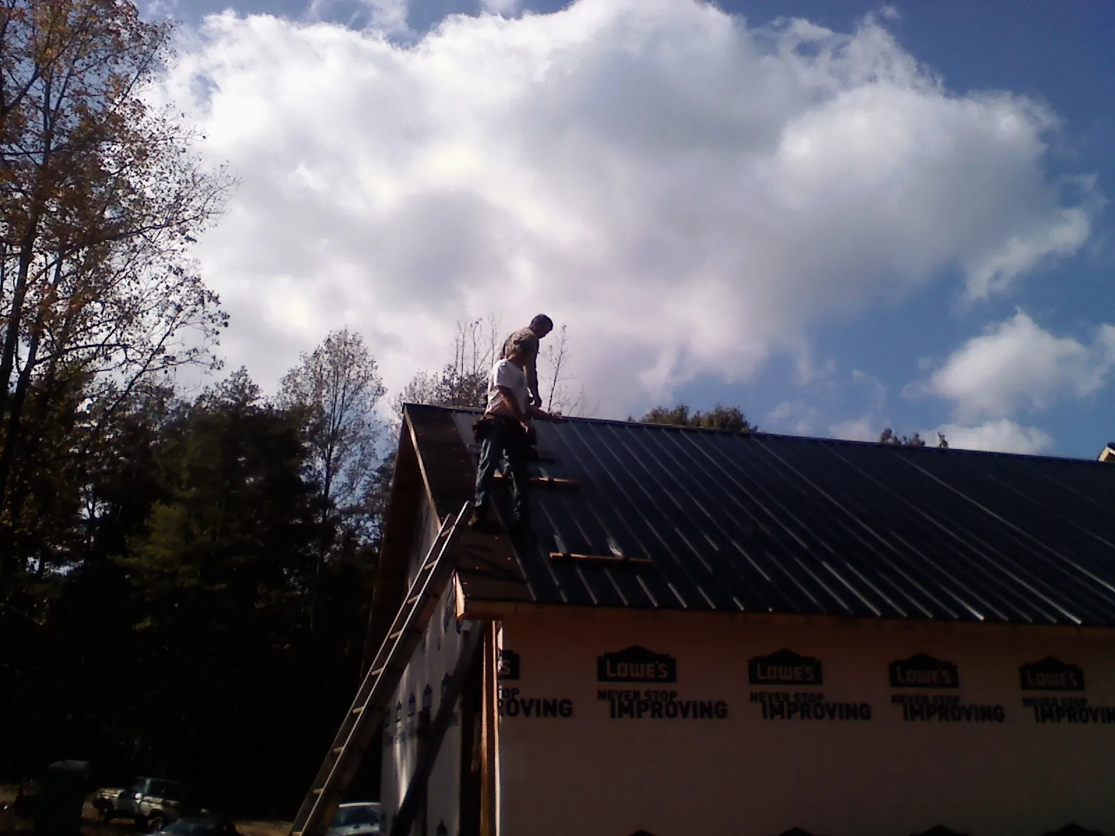 Roofer fastening dark metal panels high against a cloudy sky, from a Roof Inspection job in Creswell