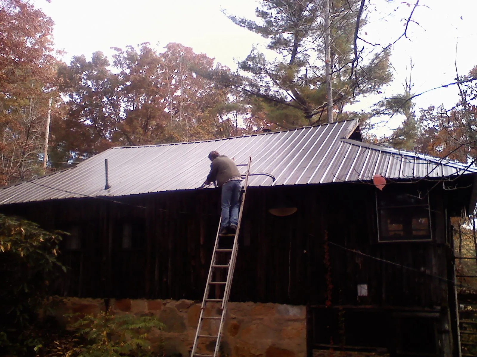 Roofer on a ladder working along the edge of a cabin metal roof in Creswell