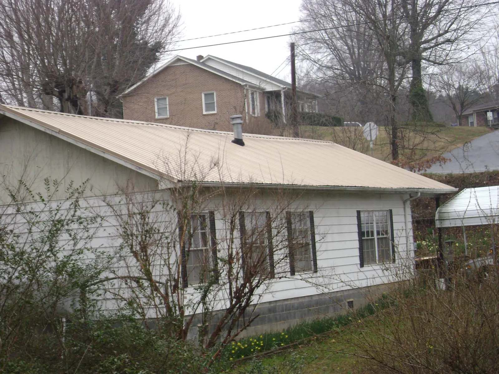 Tan metal roof on a white sided house set into a hillside — Commercial Roofing by Roofing Brothers in Creswell