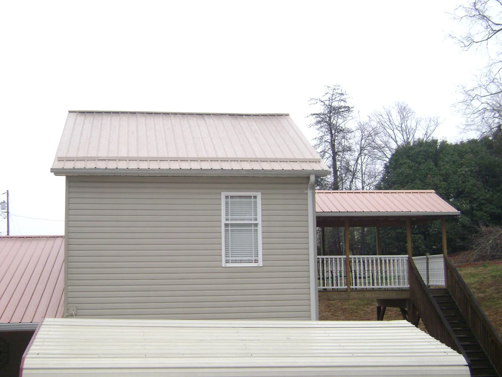 Tan metal roofs on a two story addition and attached porch, from a Roof Replacement job in Creswell